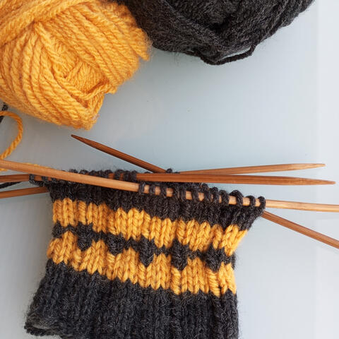 Knitting in progress of black sock with yellow details 

[material: acryl]